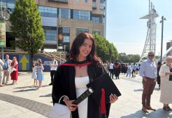 Olivia Wasp in graduation dress holding a scroll and mortarboard outside The Lowry at Salford Quays