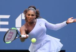 Serena Williams swings her racket towards the tennis ball with an expression of focused concentration