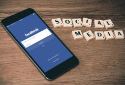 Smartphone displaying the Facebook login screen beside letter tiles spelling ‘Social Media’ on a wooden surface, representing social media and online networking.