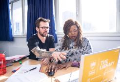 Student receiving one-to-one academic support from a member of staff while working on a laptop in the library