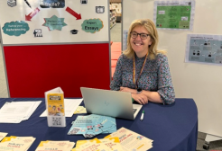 A member of library staff sitting at a table surrounded by leaflets and ready to help