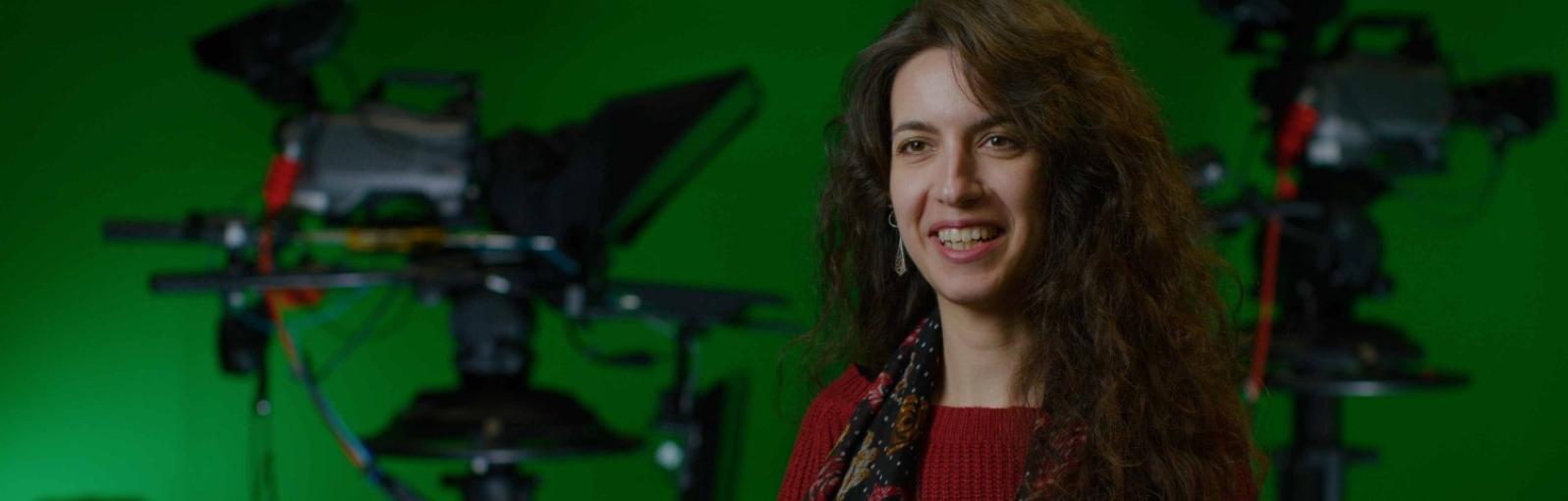A female student sits in a green screen studio in front of two cameras.