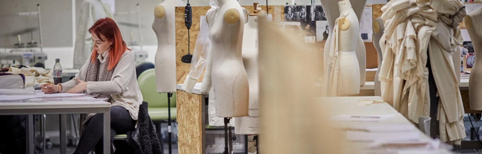 Woman working at a desk in a fashion student with mannequins around her 