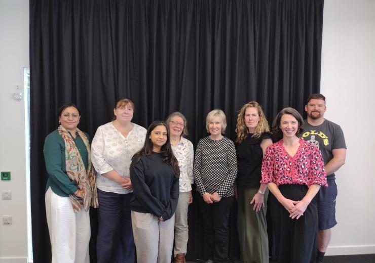 This image shows a group of people standing in front of a dark curtain