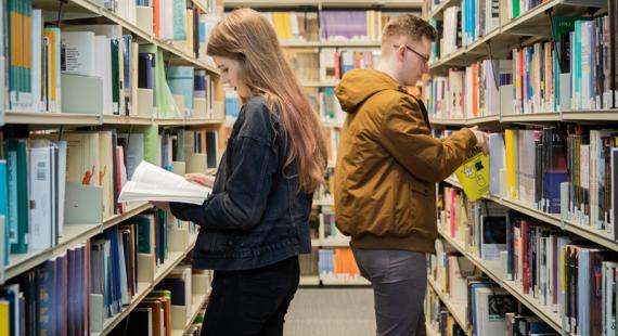 Two students selecting books from shelves in Clifford Whitworth Library