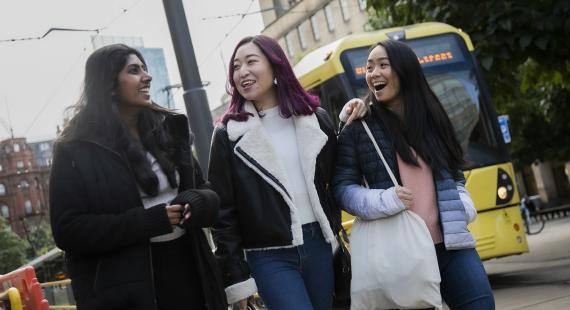 Three students walking around Manchester city centre alongside a tram