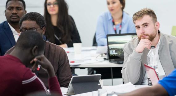 Six students in a lecture with laptops, tablets and note books
