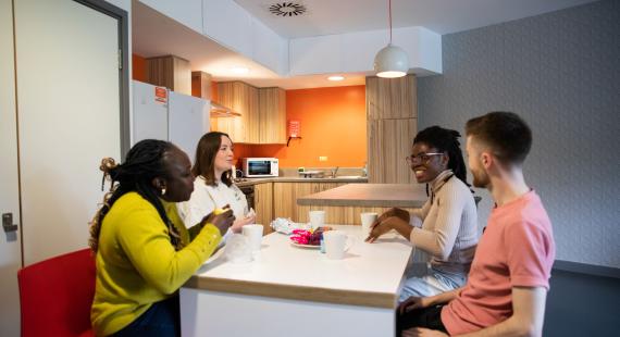 Group of four students sitting round a kitchen table eating and drinking