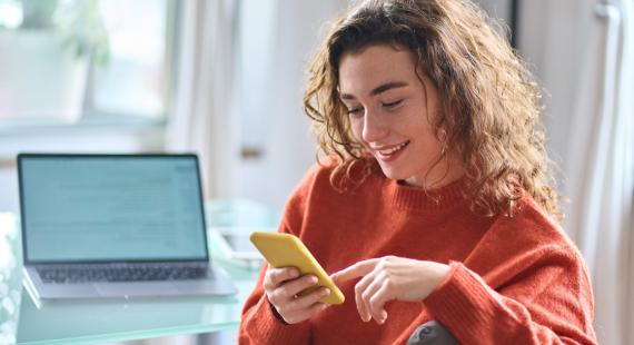 Woman using her smartphone besides a laptop on a table