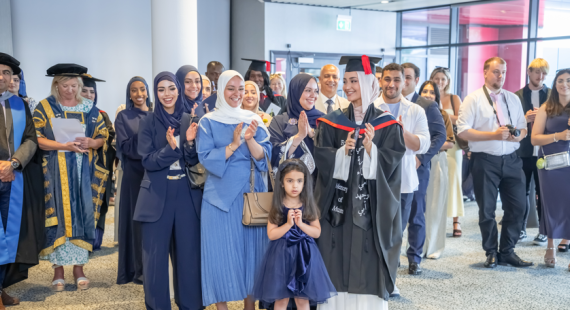 A crowd of people at a graduation ceremony, including graduates in black caps and gowns