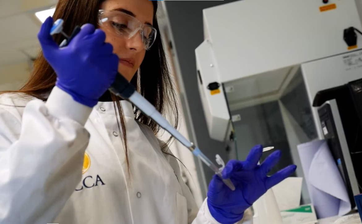 A lady in a white lab coat is holding a pipette