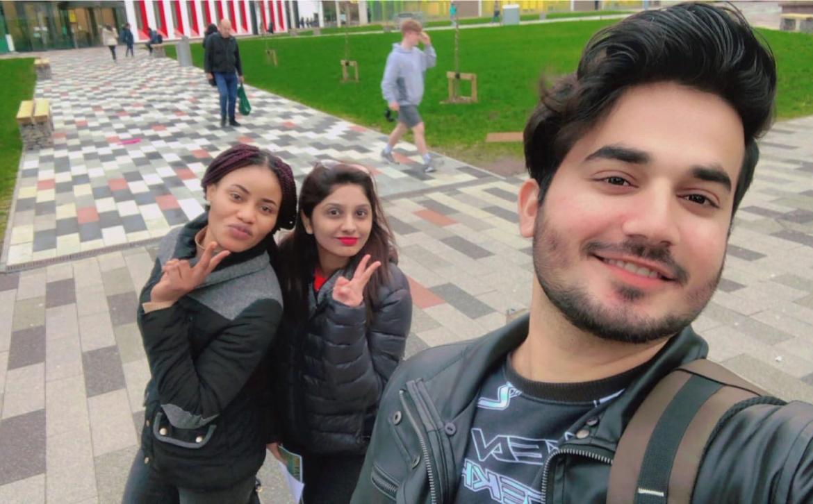 Man taking selfie outside with two women posing behind him. 