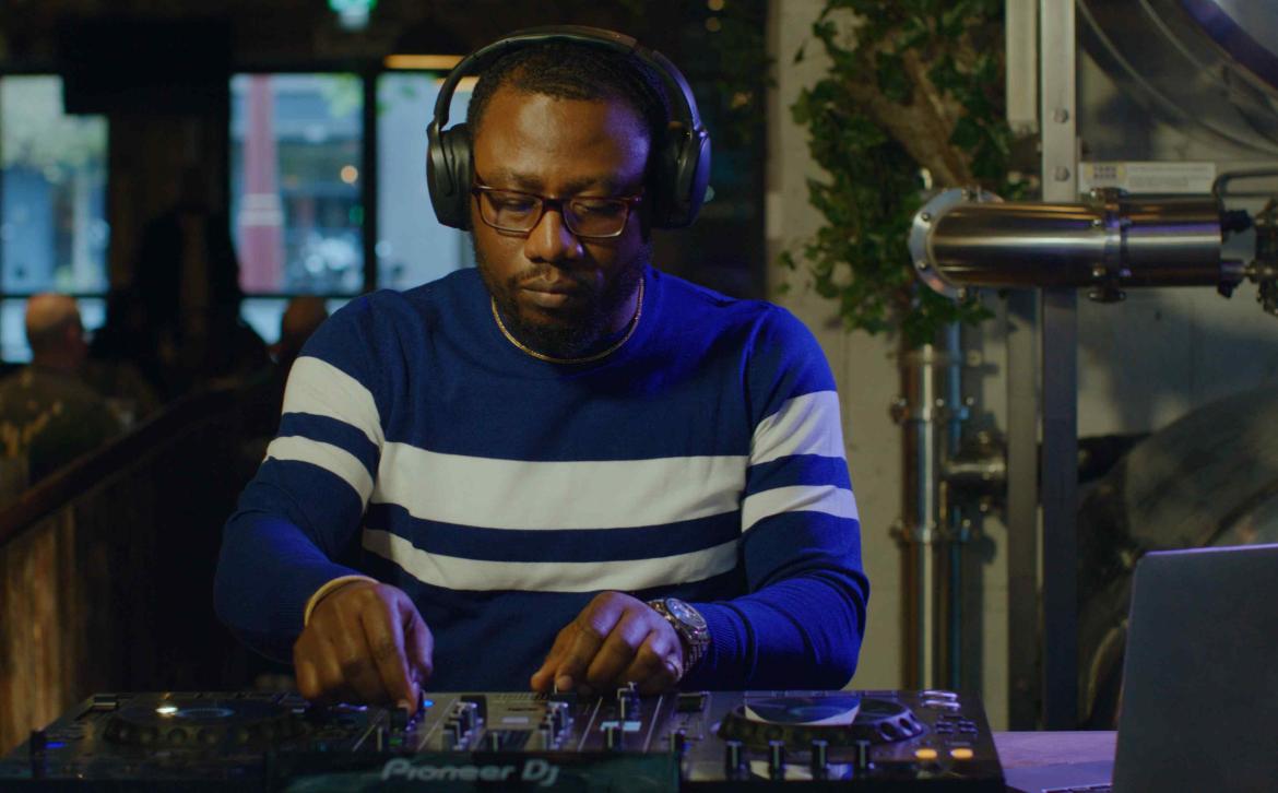 A man in a blue and white striped sweater on DJ decks