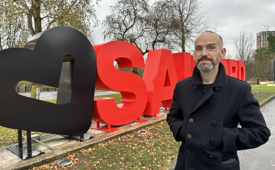 A man stands in front of the love salford sign