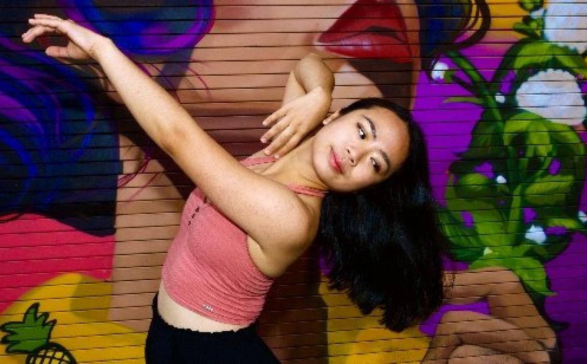 A student in front of a graffiti wall dancing 