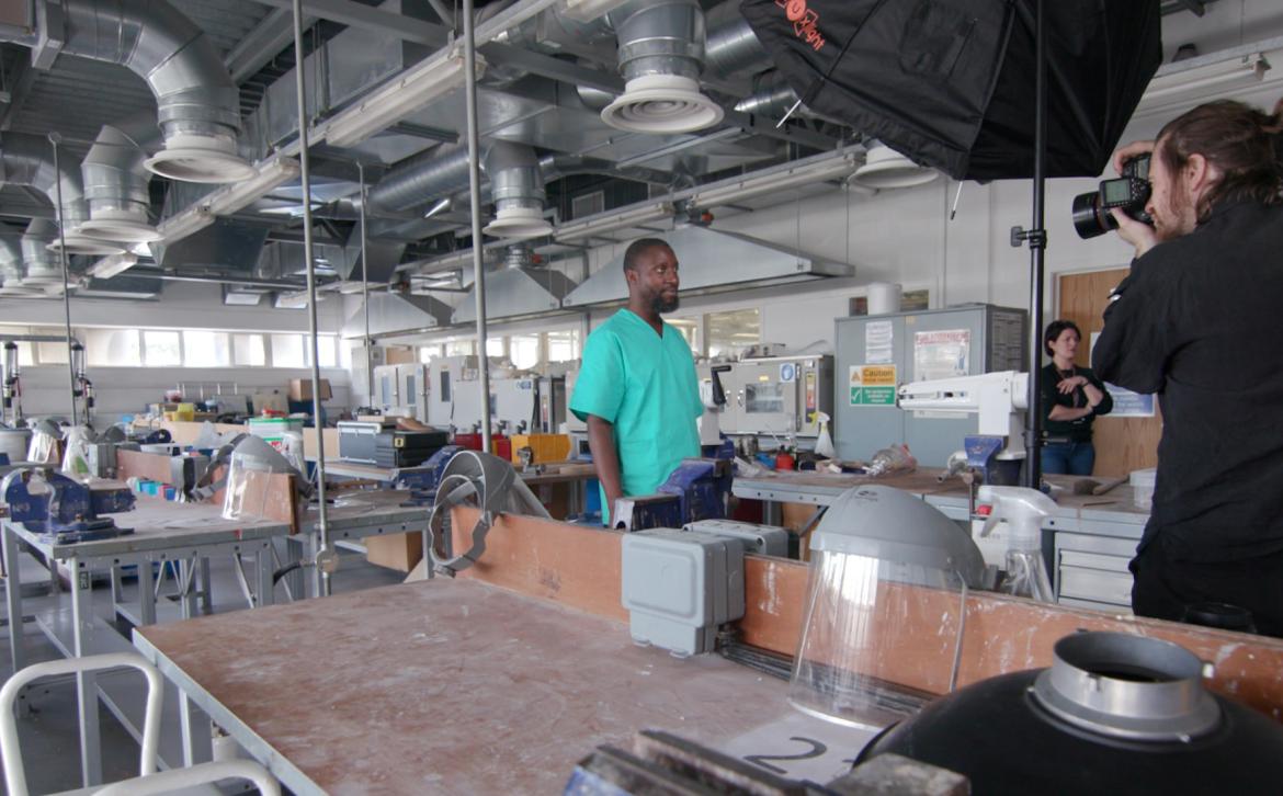A photographer taking a photograph of Timothy Isingoma in the prosthetics workshop