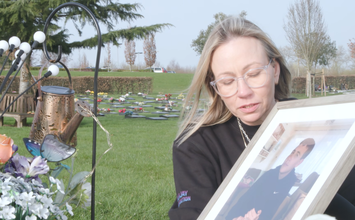 A woman holds a photo of her son next to a grave